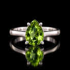 The same VooDooStone pear-cut solitaire ring turning peridot green under fluorescent light, front view. Item 894782.