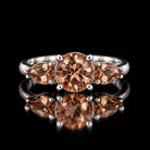 The same VooDooStone three-stone ring turning golden amber under warm incandescent light, front view. Item 894786.